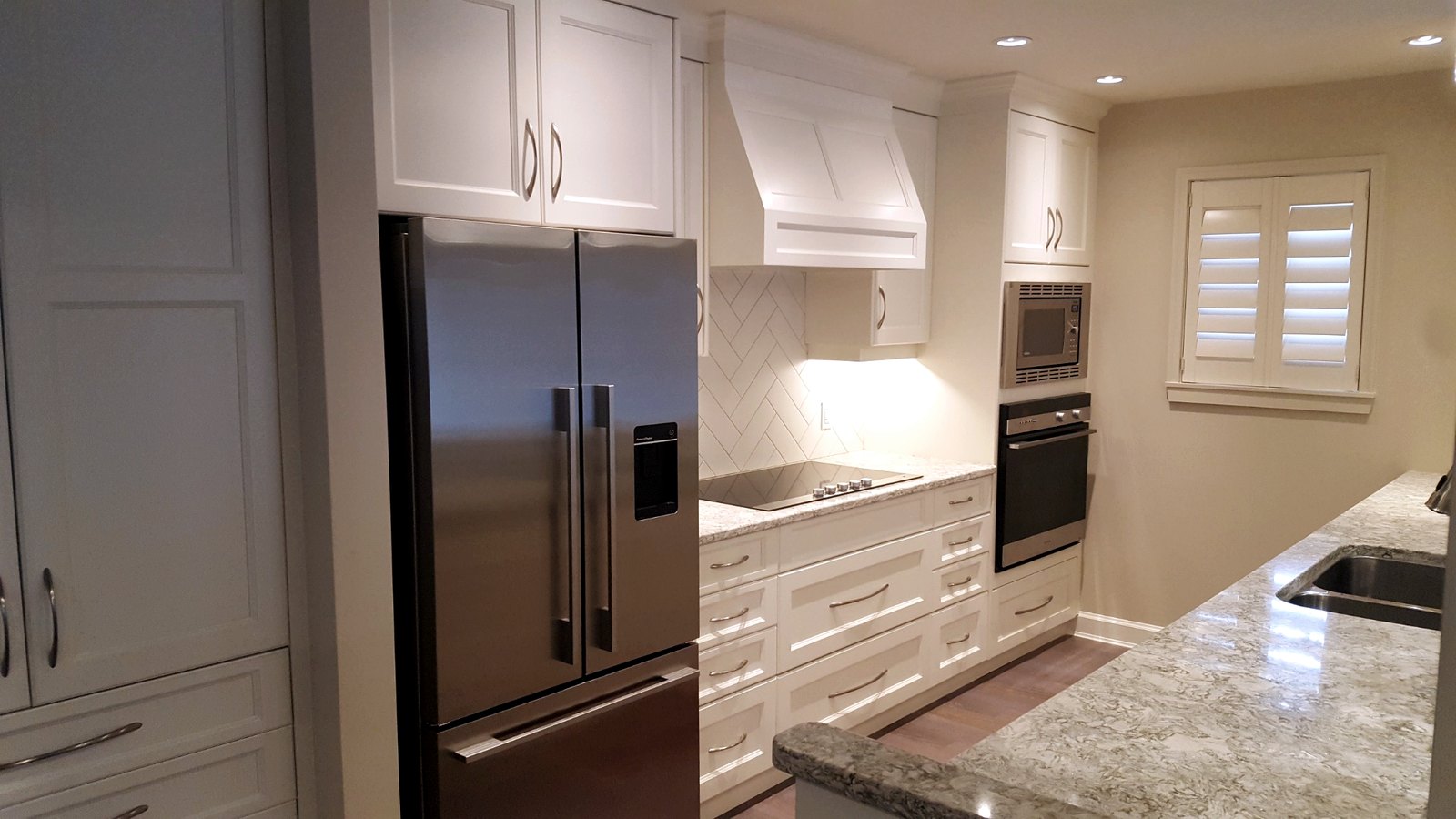 Open-concept white kitchen with stone countertops, stainless steel appliances, and improved sightlines as part of a whole-home addition.