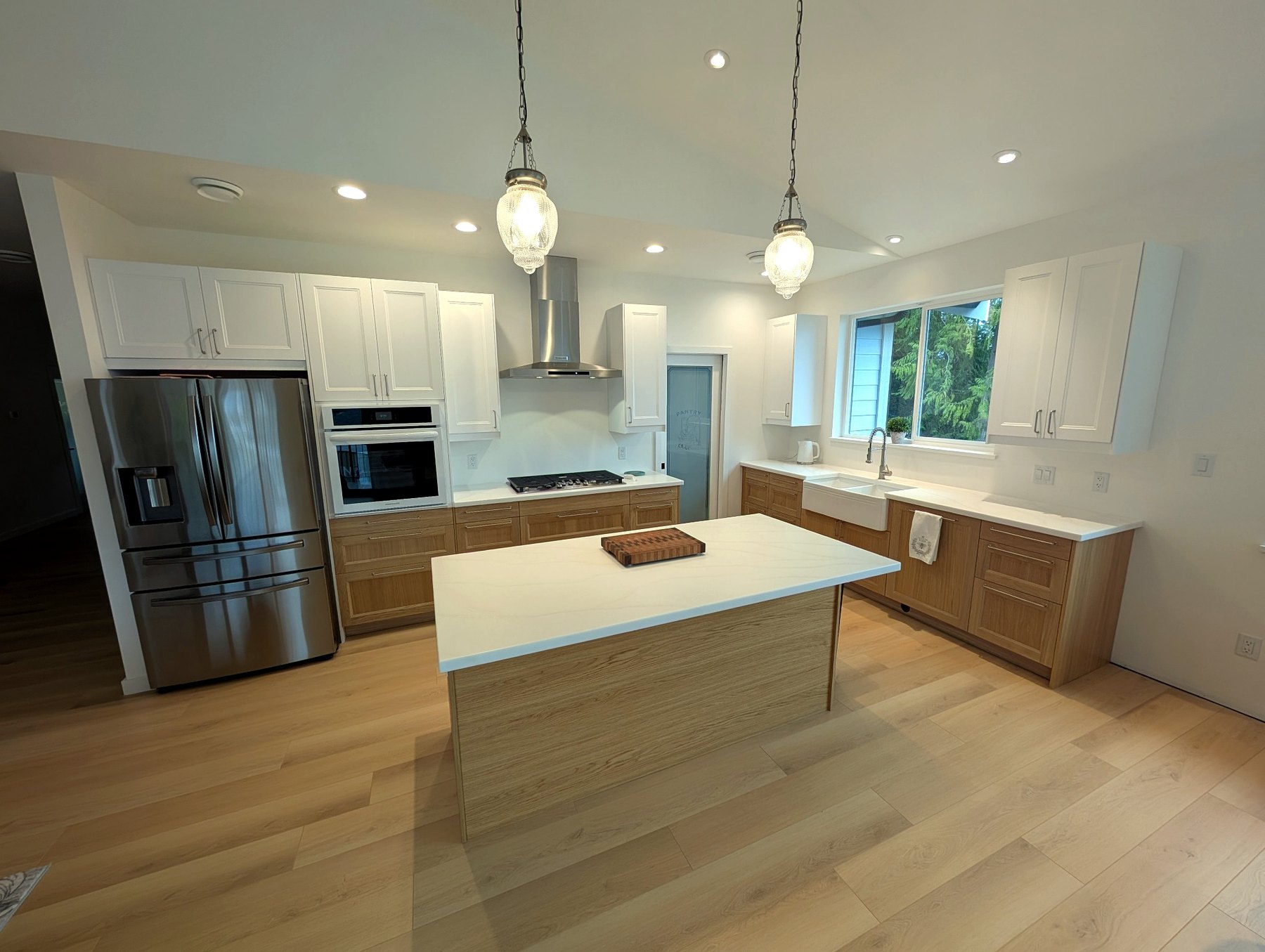 Bright custom IKEA kitchen featuring a large island, quartz countertops, shaker-style upper cabinetry, and warm wood lower cabinets.