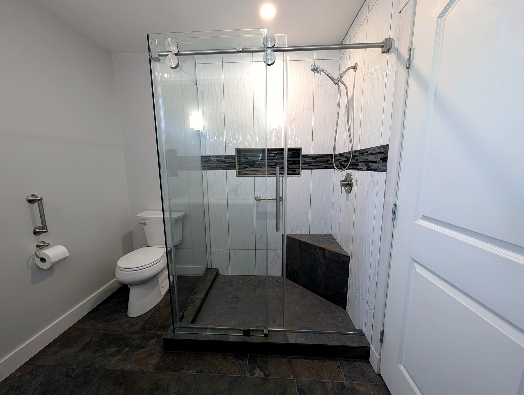 Custom walk-in shower with glass sliding doors and tiled bench.