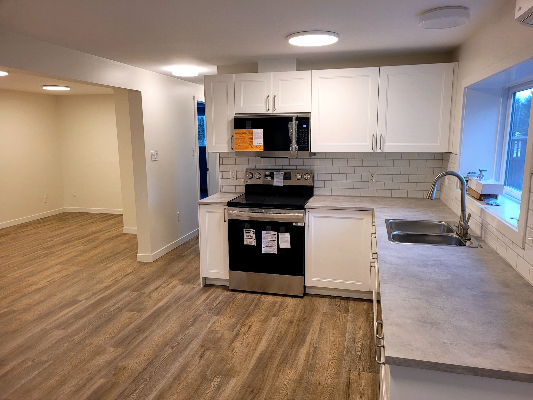 Bright open-concept kitchen and living area featuring custom cabinetry, subway tile backsplash, and durable luxury vinyl flooring throughout.